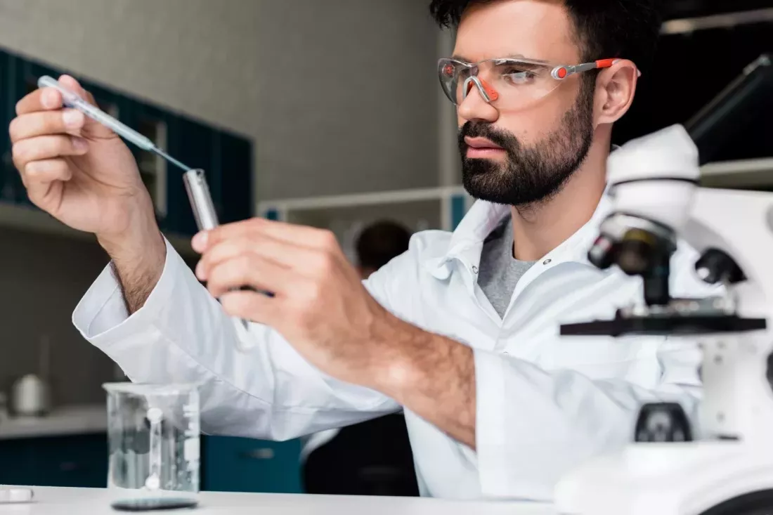 Ricercatore con occhiali protettivi versa con una pipetta un campione in una provetta in un laboratorio di chimica