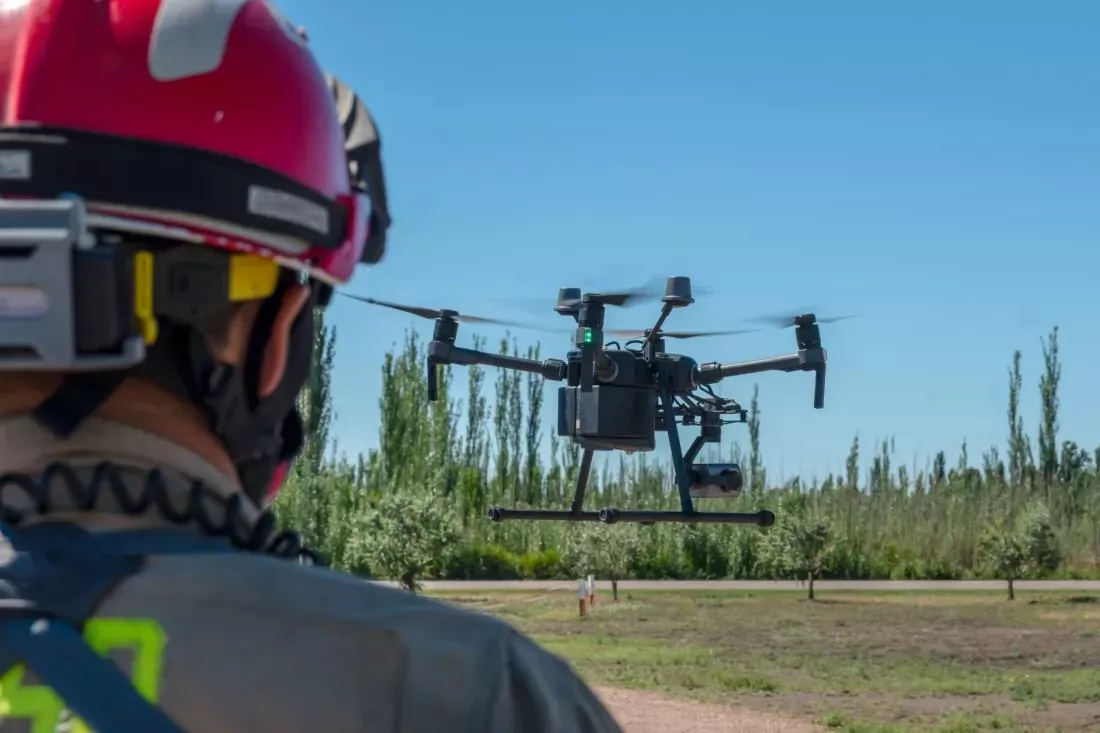 Vigile del fuoco con casco osserva un drone in volo sopra un campo