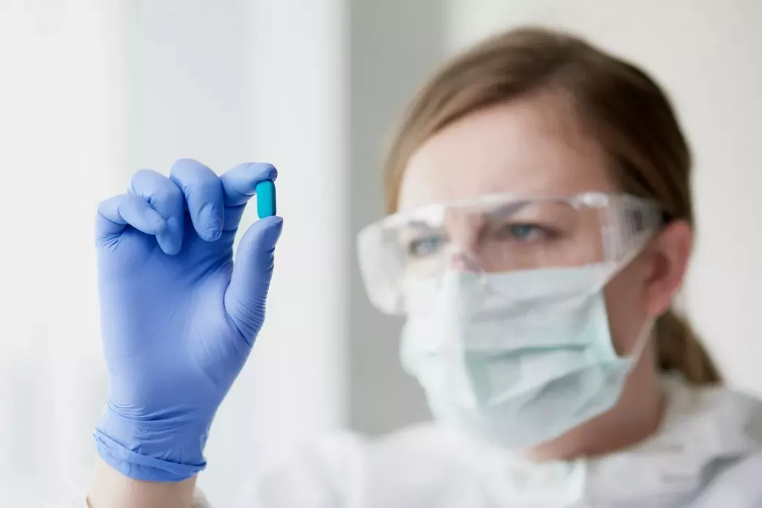 Una tecnica di laboratorio con occhiali protettivi e mascherina osserva una capsula blu.