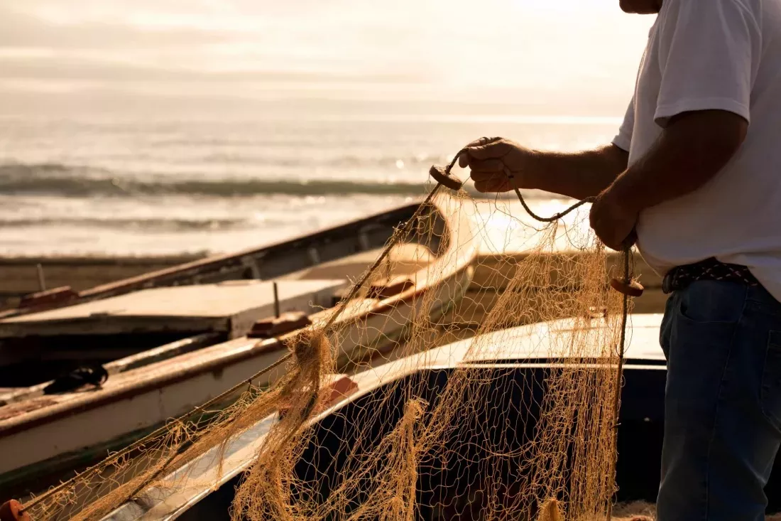 Pescatore districa una rete da pesca accanto alle barche sulla spiaggia al tramonto
