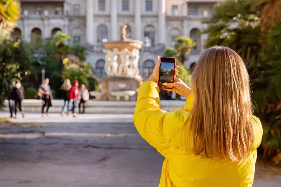 Giovane donna con giacca gialla fotografa una piazza con il cellulare